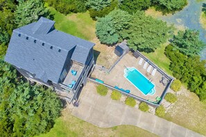 Vista aérea de uma casa com piscina, cercada por árvores e um gramado bem cuidado.
