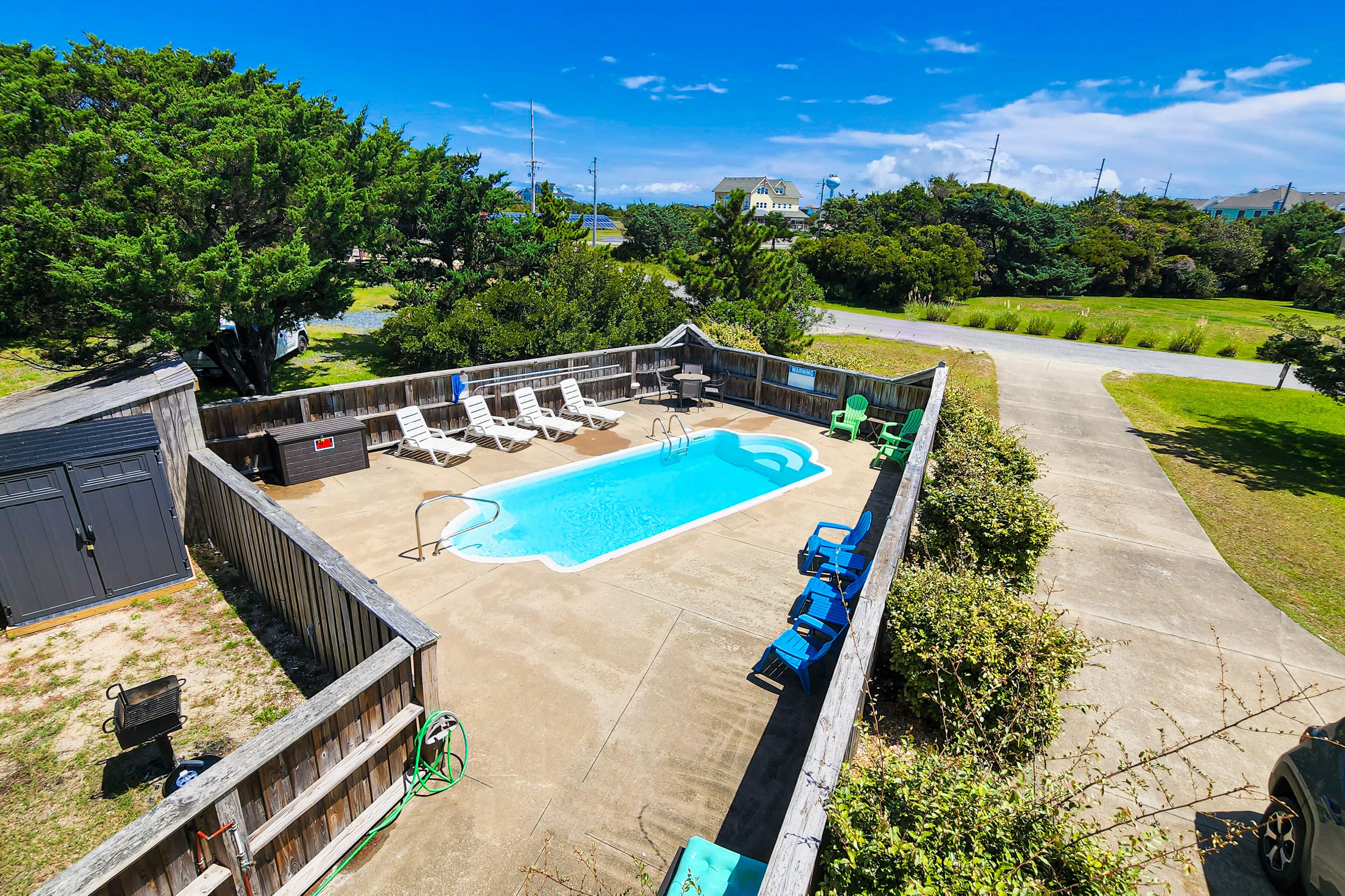 A backyard with a swimming pool, lounge chairs, and a barbecue area.