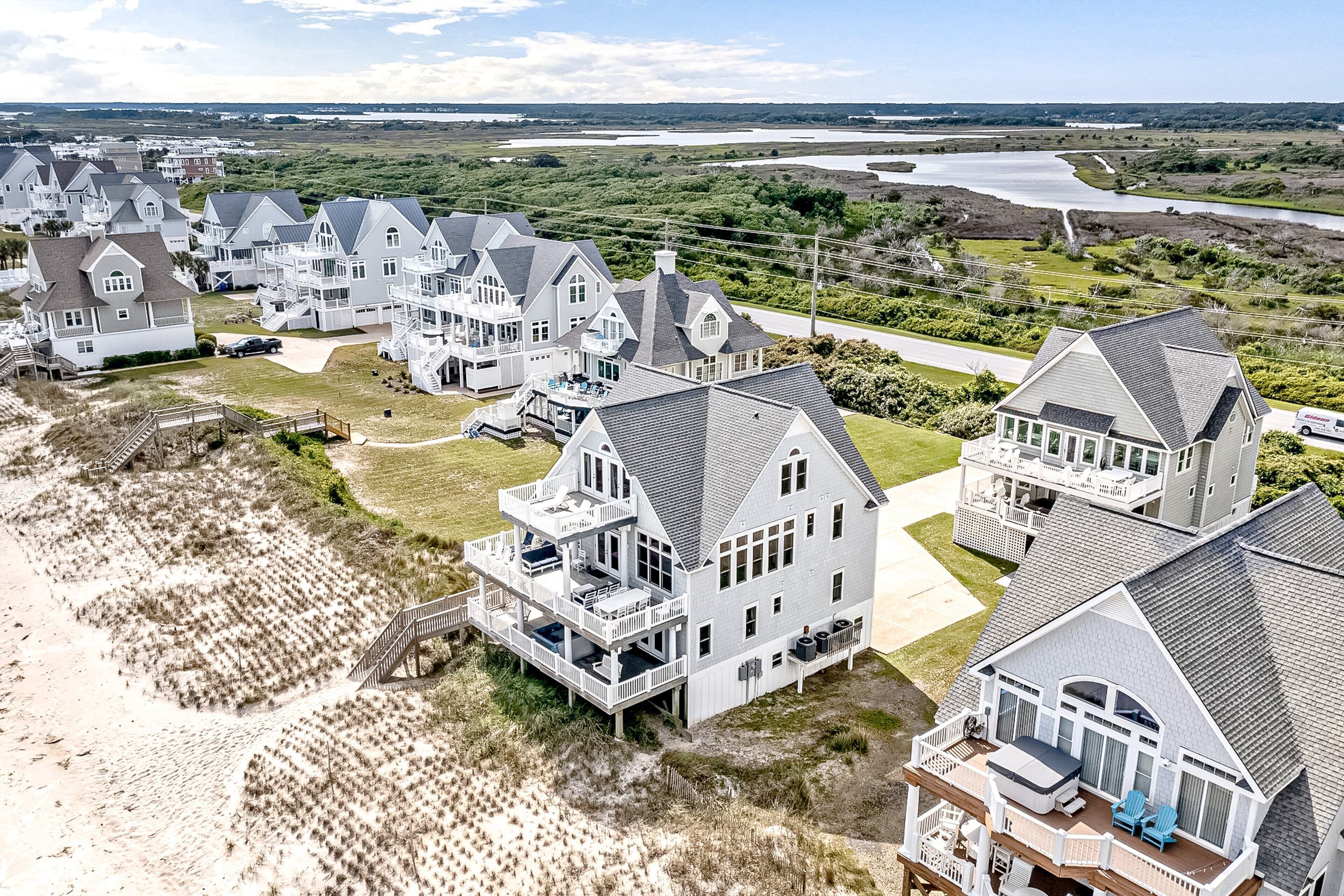 A coastal residential area with multiple houses featuring large balconies, some with outdoor seating, and a sandy beach in the foreground.