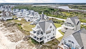 Zona residencial costera con varias casas que tienen balcones amplios, algunos con mobiliario exterior, y una playa de arena al frente.