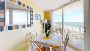 A room with a balcony, a table with chairs, a plant, and a view of the beach. - Oceanfront condo with pool, sauna, gym, game room, on-site restaurants, balcony (North Topsail Beach)