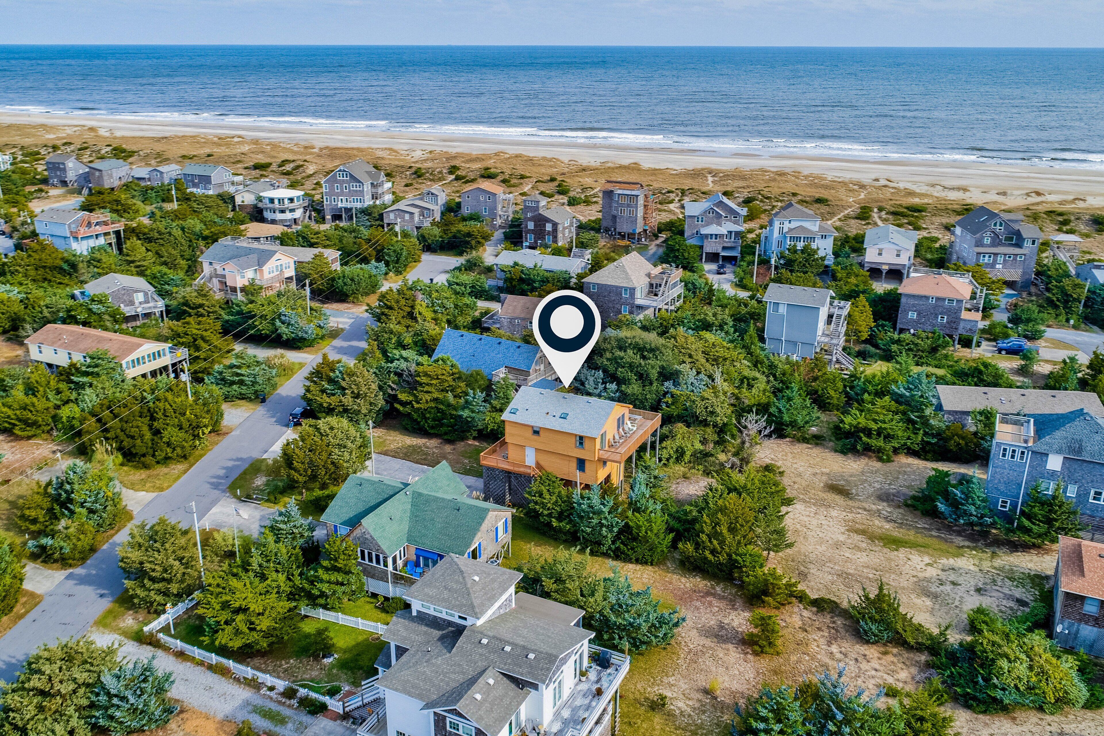 Vue aérienne d’une zone résidentielle côtière, avec des maisons, une plage et un point de repère clairement identifiable.