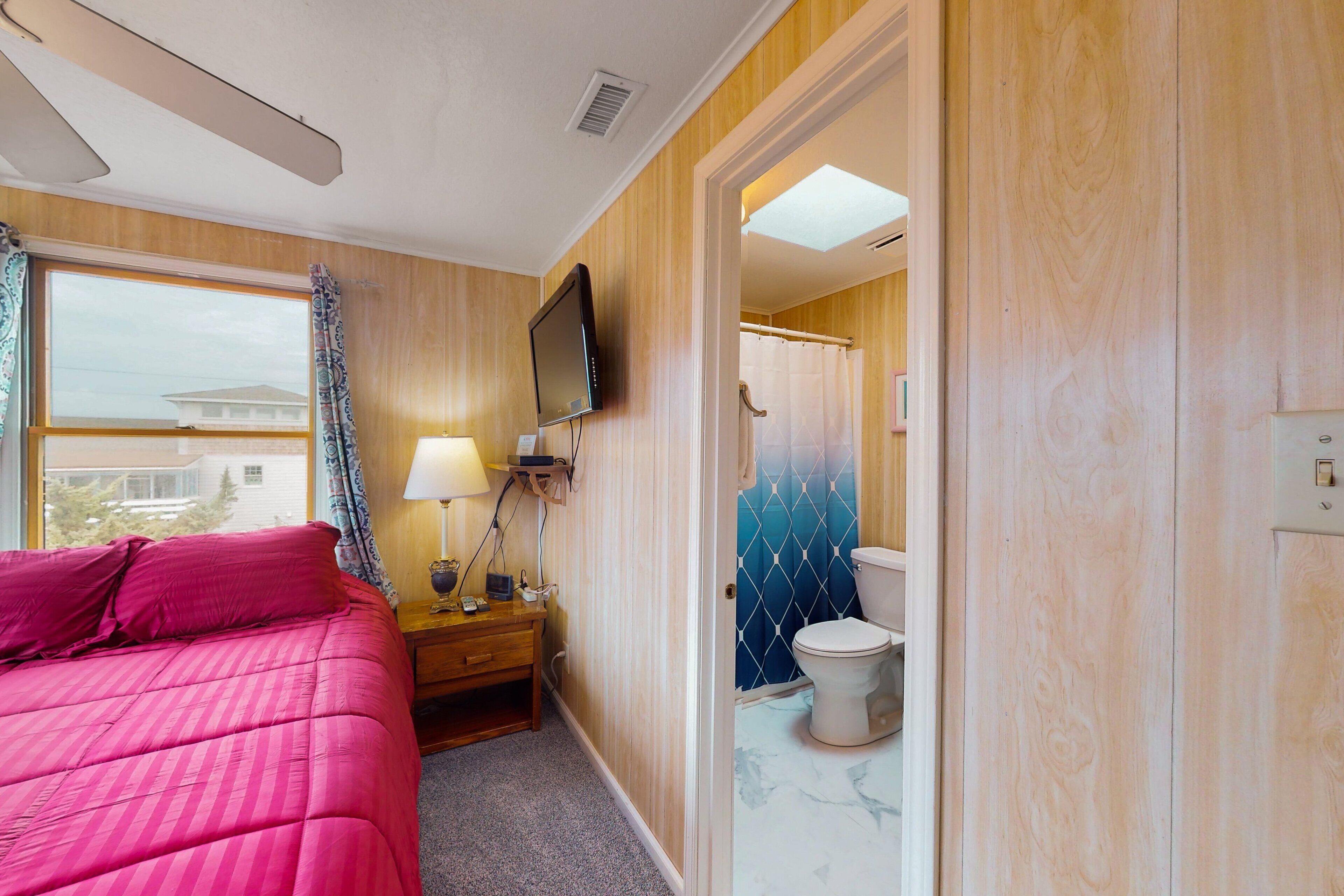 Un dormitorio con cama, mesita de noche, televisión y ventana con cortinas.