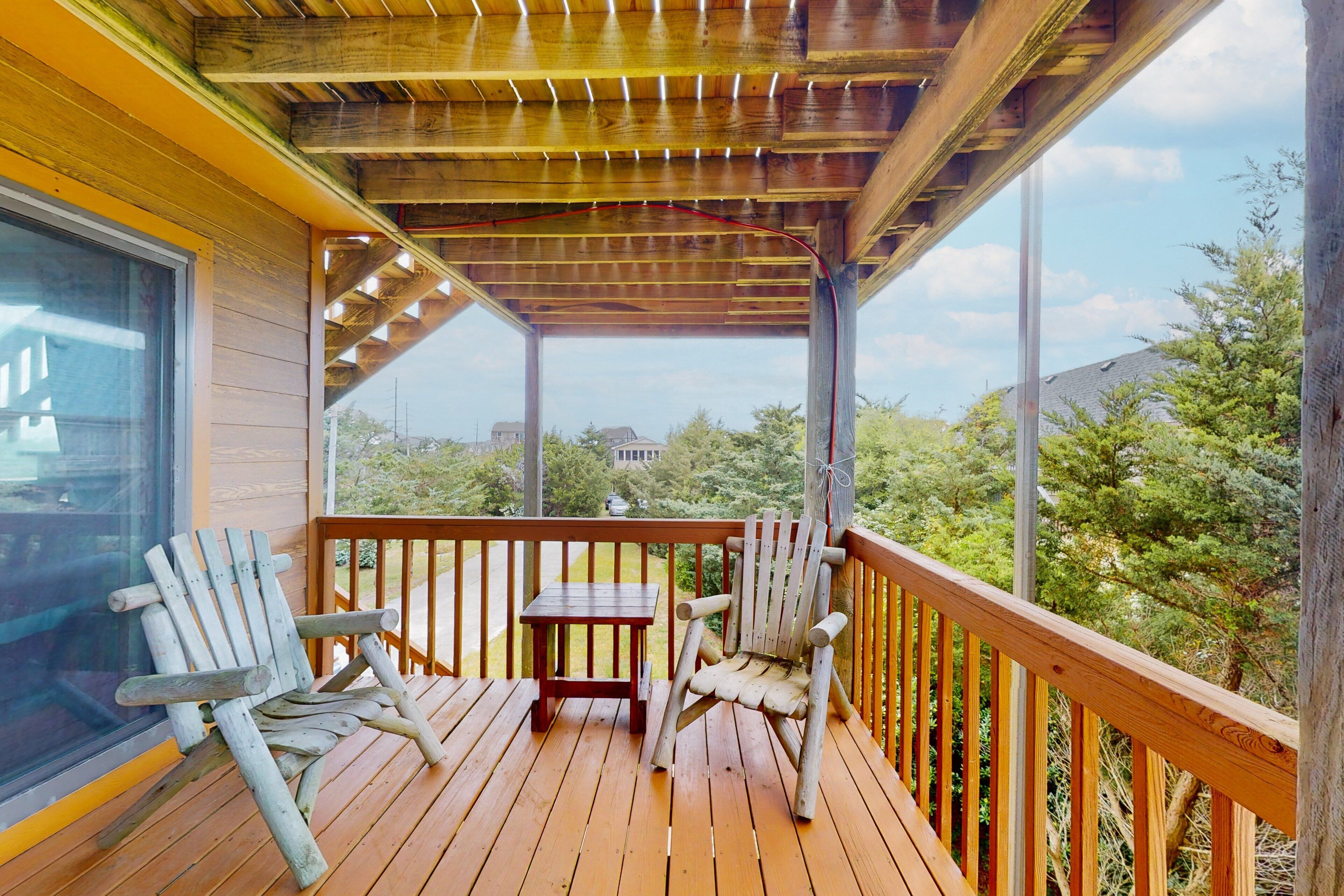 A wooden deck with two Adirondack chairs and a small table, overlooking a residential area with trees and houses.