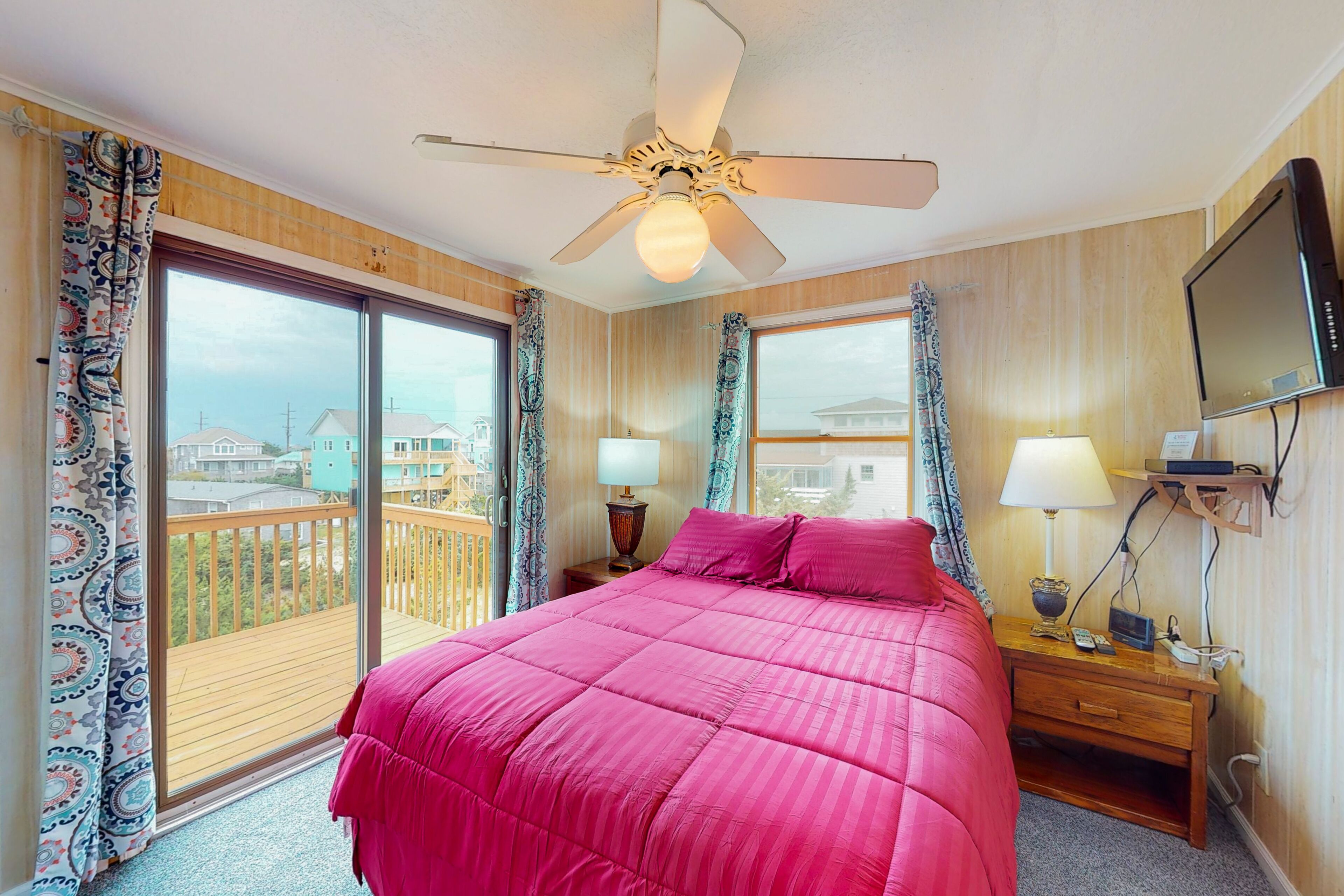 A hotel room with a large bed, a ceiling fan, a TV, and a balcony with a view of the city.