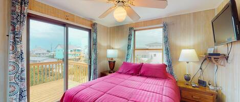 A hotel room with a large bed, a ceiling fan, a TV, and a balcony with a view of the city.