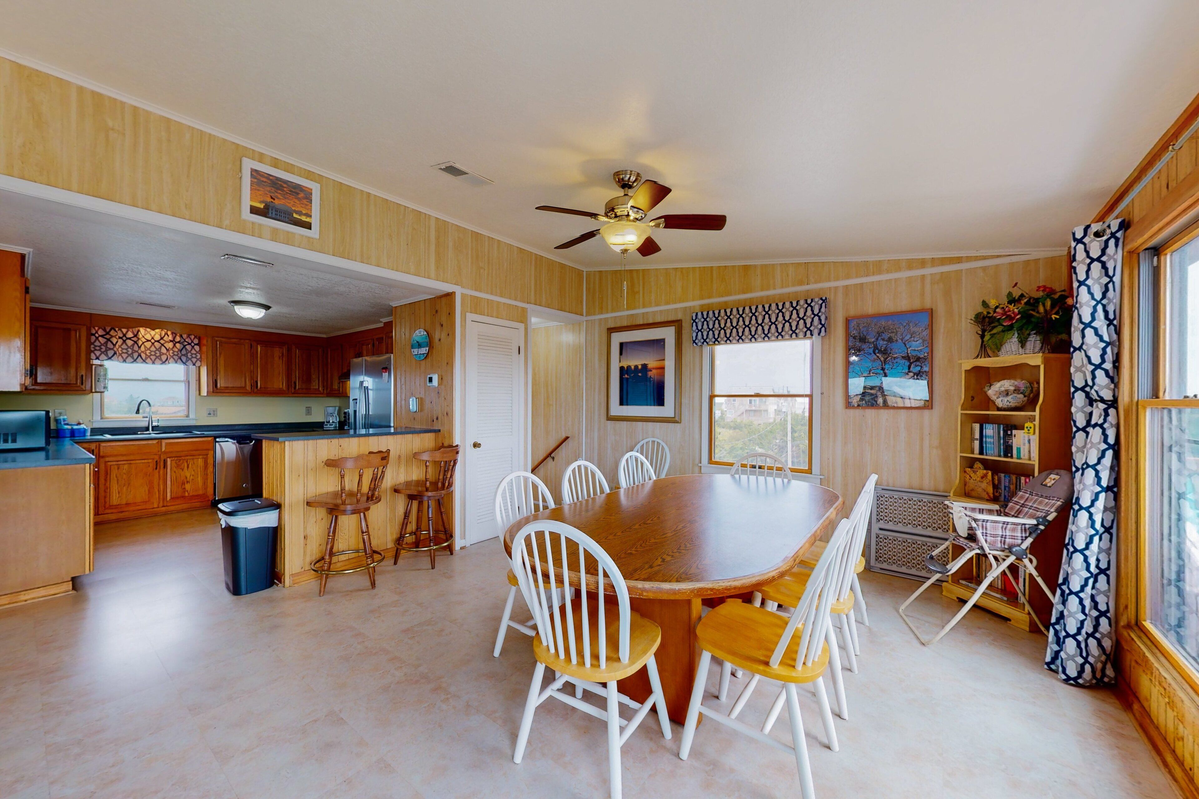 A spacious kitchen with wooden cabinets, a dining table with white chairs, and a ceiling fan.