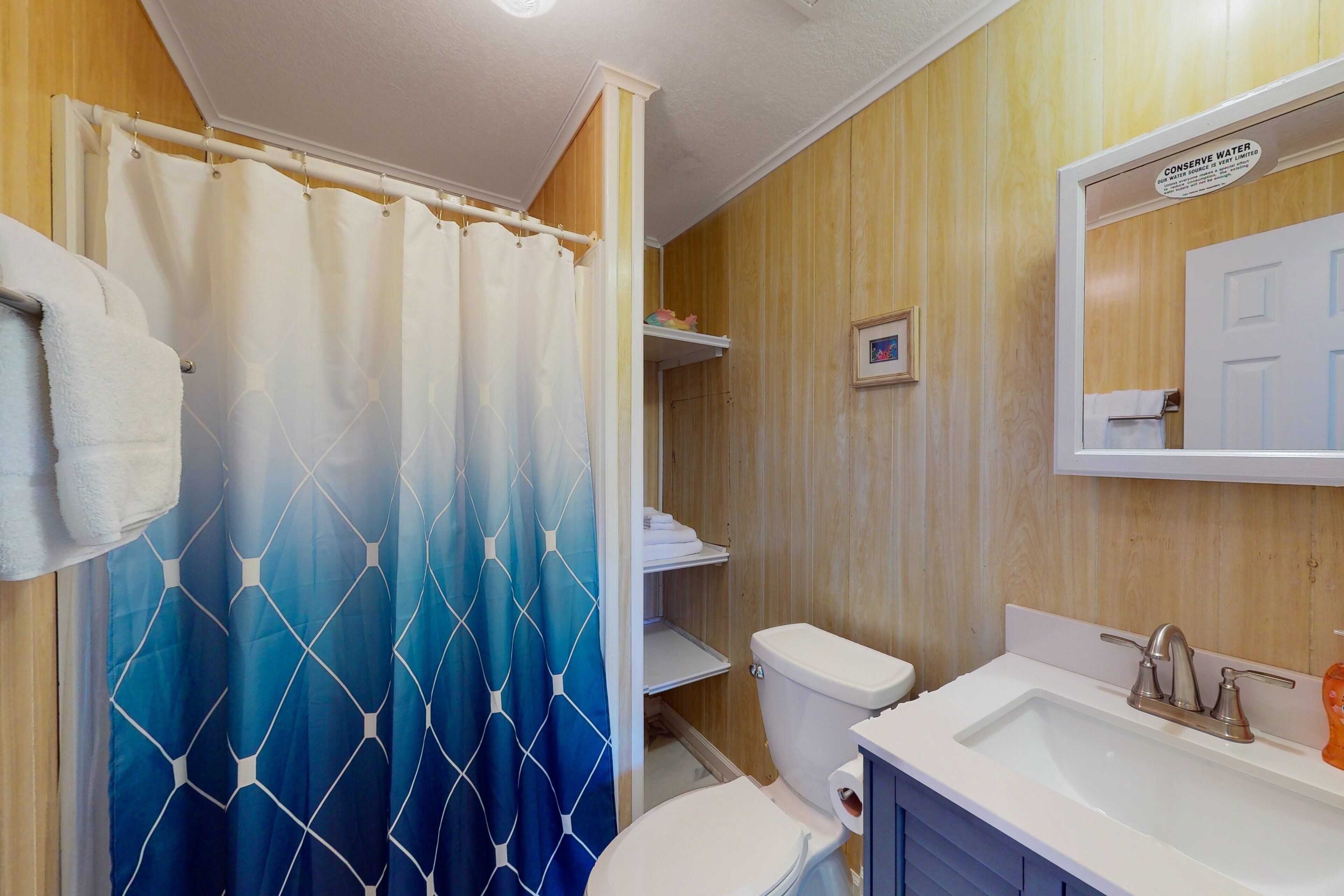 A bathroom with a shower curtain, toilet, sink, and a 'Conserve Water' sign.