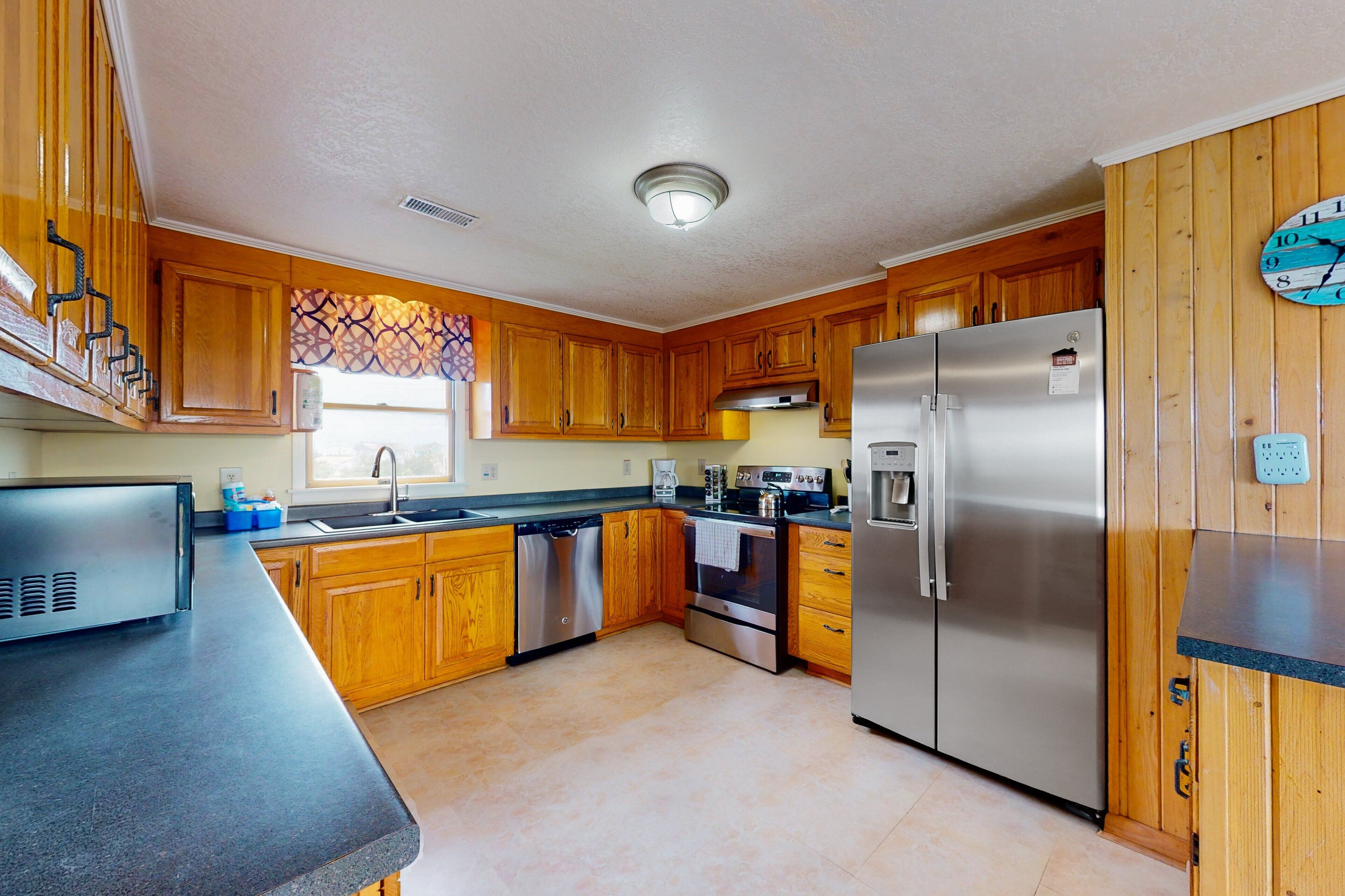A kitchen with wooden cabinets, stainless steel appliances, a dishwasher, and a clock on the wall.