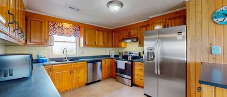 A kitchen with wooden cabinets, stainless steel appliances, a dishwasher, and a clock on the wall.