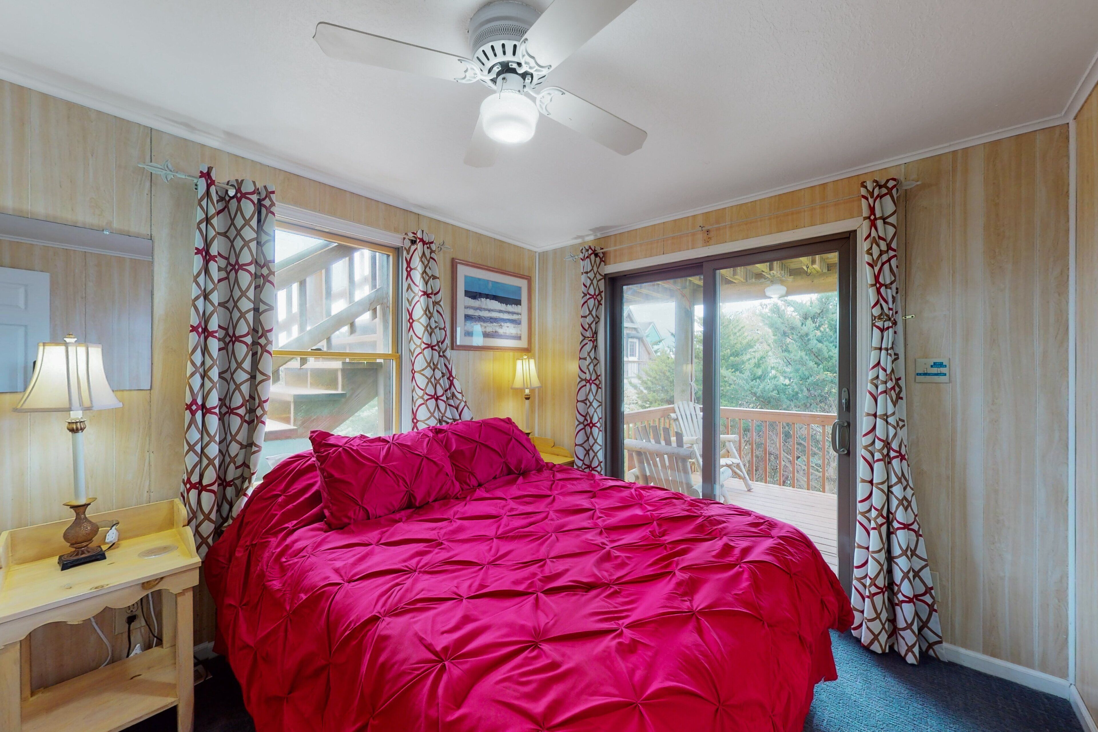 A bedroom with a bed, a desk, a chair, a ceiling fan, and a balcony with curtains.
