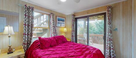 A bedroom with a bed, a desk, a chair, a ceiling fan, and a balcony with curtains.