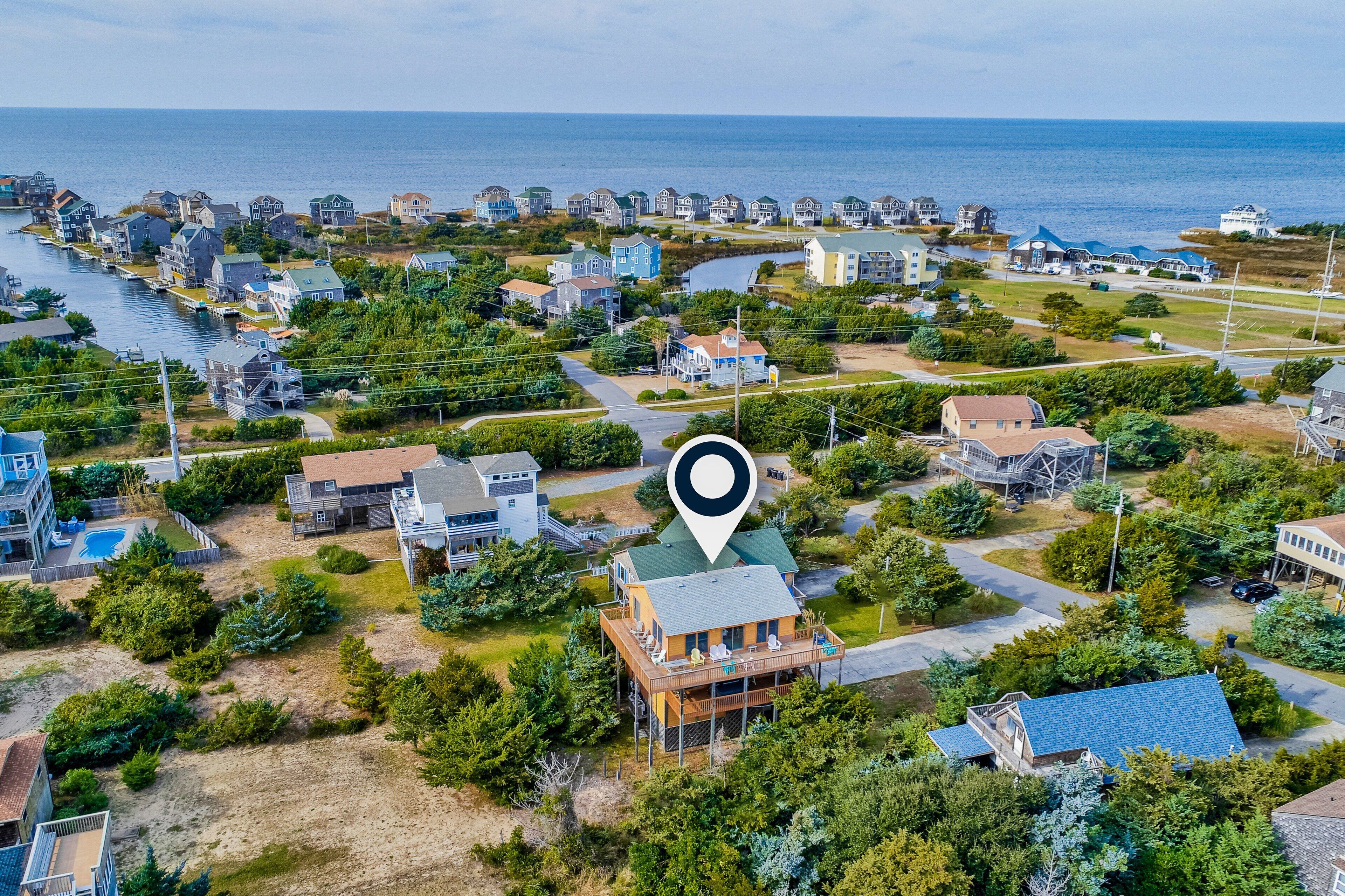 An aerial view of a coastal residential area with houses, a body of water, and a prominent location marker.