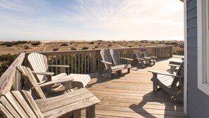 A wooden deck with Adirondack chairs and a table, overlooking a beach. - Beautiful dog-friendly home overlooking the beach with hot tub, WiFi, & AC (Salvo)