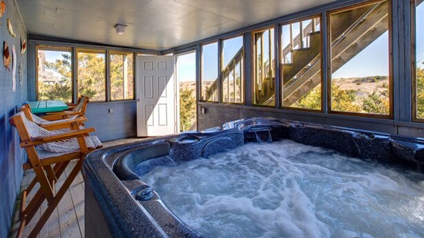A hot tub area with wooden chairs, a door, and large windows overlooking a natural landscape. - Beautiful dog-friendly home overlooking the beach with hot tub, WiFi, & AC (Salvo)