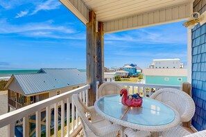 Ein Balkon mit Korbmöbeln und einem Glastisch, mit Blick auf einen Strand und weitere Gebäude.