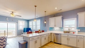 Una cocina moderna con armarios blancos, lavavajillas de acero inoxidable, luces colgantes y vistas al exterior.