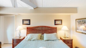 A neatly made bed with a folded towel, two bedside lamps, and framed pictures on the walls. - Family Condo w/Free WiFi, Central AC, Shared Pool, Private Washer/Dryer (Hatteras)