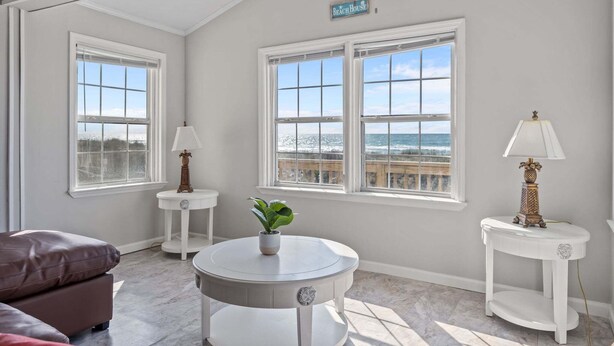 Ein Zimmer mit Deckenventilator, zwei Fenstern mit Blick, einem kleinen Tisch mit Pflanze und einer Lampe auf einem Beistelltisch.