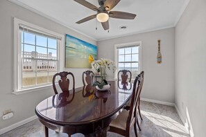 A dining room with a round table, chairs, a ceiling fan, and large windows. - Ocean-view home with stunning views and beach access across the street — 2026 New Upgrades! (North Topsail Beach)