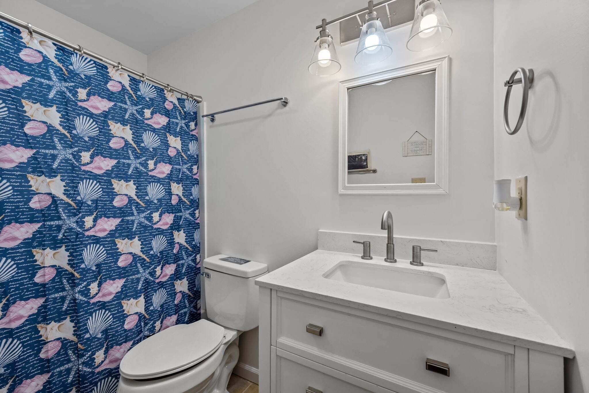 Un baño con inodoro, lavabo, espejo y cortina de ducha.