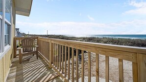 Eine Holzterrasse mit einem Stuhl, mit Blick auf einen Strand mit Dünen und dem Meer.