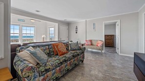 Ein großzügiges Wohnzimmer mit einer großen Couch, einem Essbereich und Meerblick durch große Fenster.