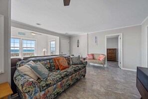 A spacious living room with a large sofa, a dining area, and a view of the ocean through large windows. - Ocean-view home with stunning views and beach access across the street — 2026 New Upgrades! (North Topsail Beach)