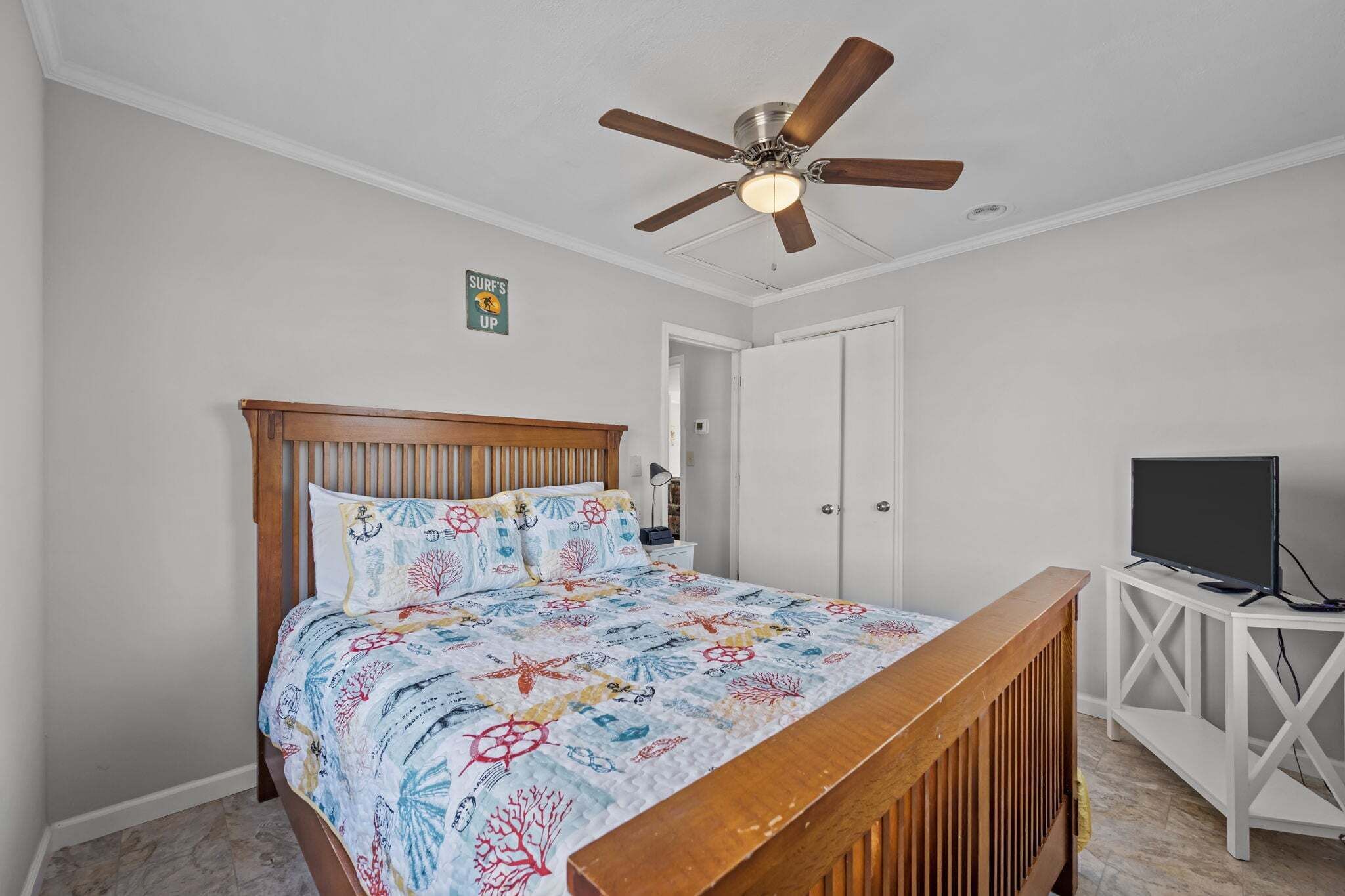 Un dormitorio con cama, ventilador de techo, televisor sobre un mueble y una puerta.