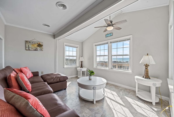 A spacious living room with a brown leather sofa, a round white coffee table, and a ceiling fan.