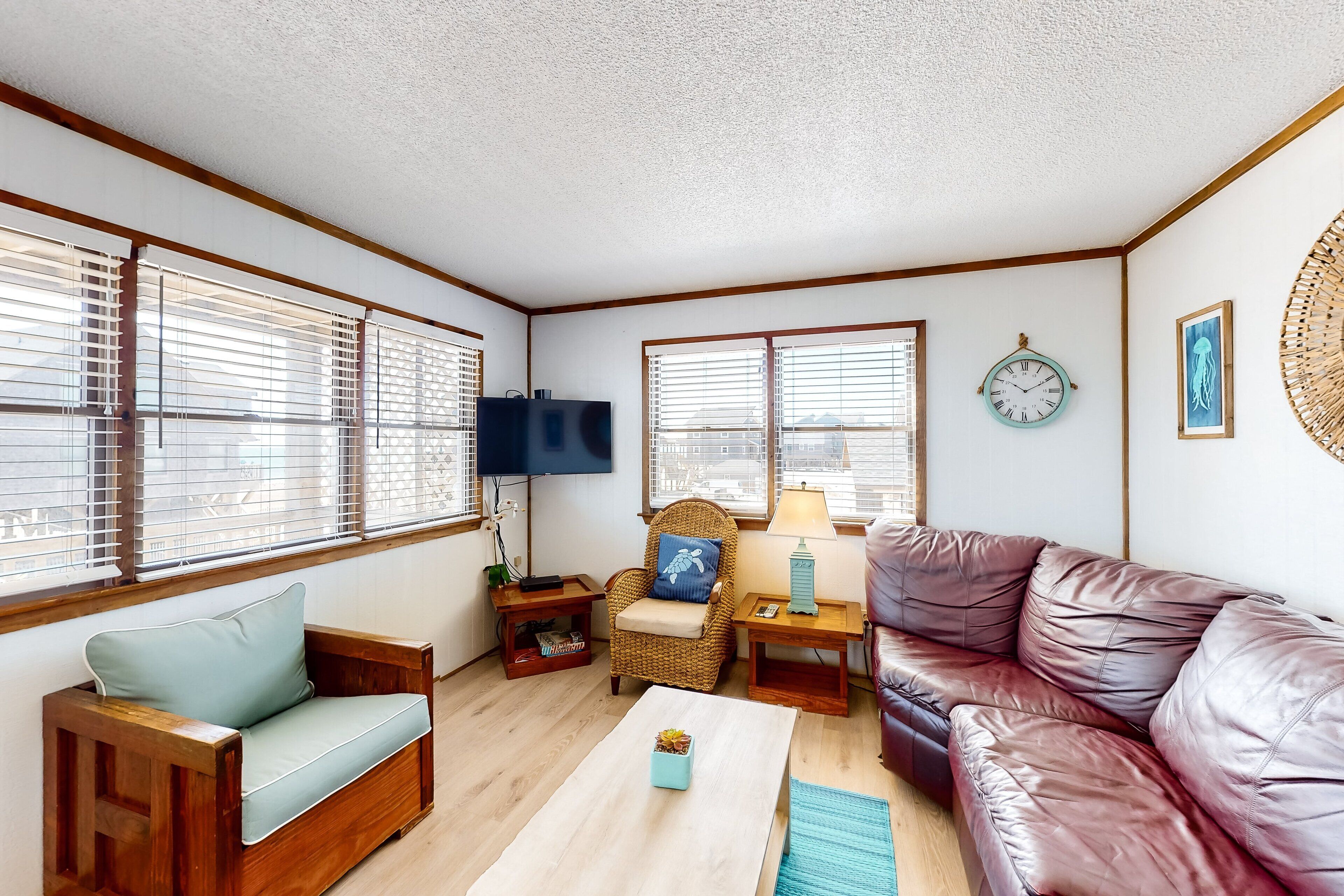 A cozy living room with a wooden sofa, a leather couch, and a wicker chair. There is a flat-screen TV, a lamp, and a clock on the wall.