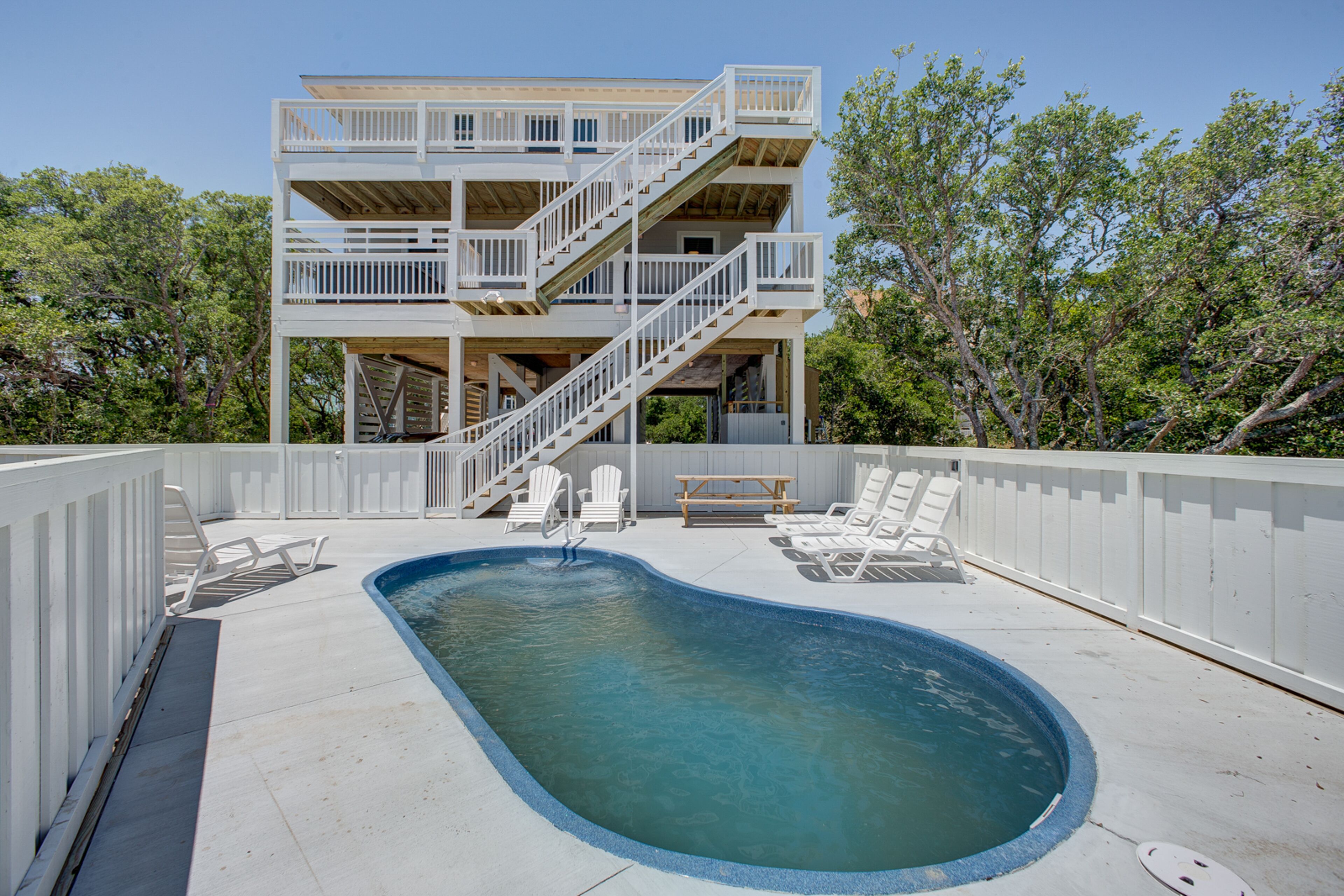 Un bâtiment à deux étages doté d’une piscine, de chaises longues et d’un escalier.