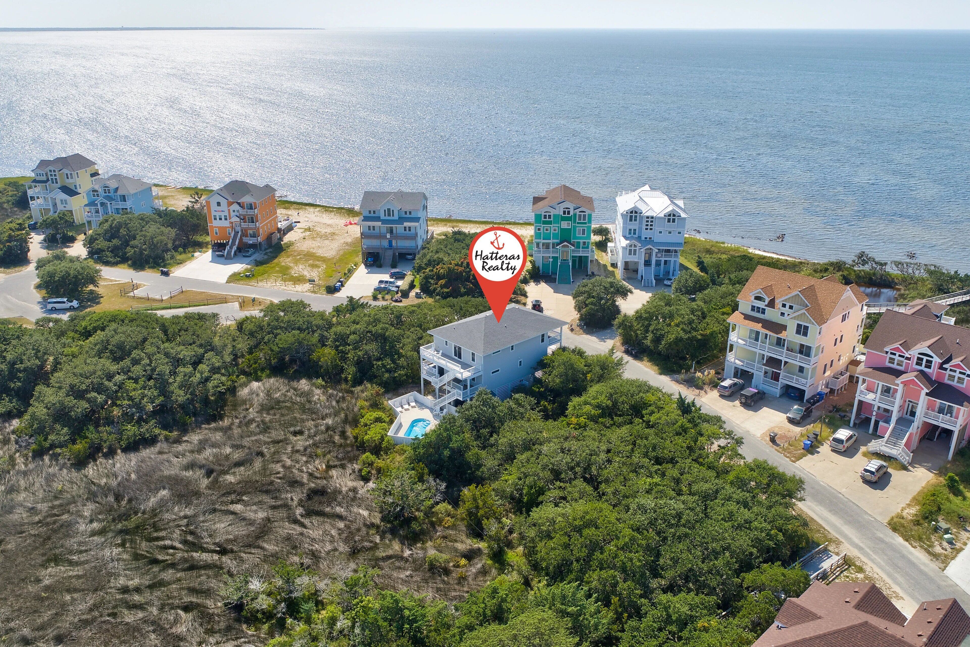 An aerial view of a coastal residential area with multiple two-story houses, a swimming pool, and a beach in the background.