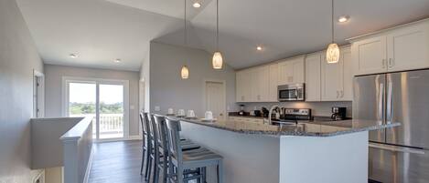 A modern kitchen with a large island, stainless steel appliances, and pendant lighting.