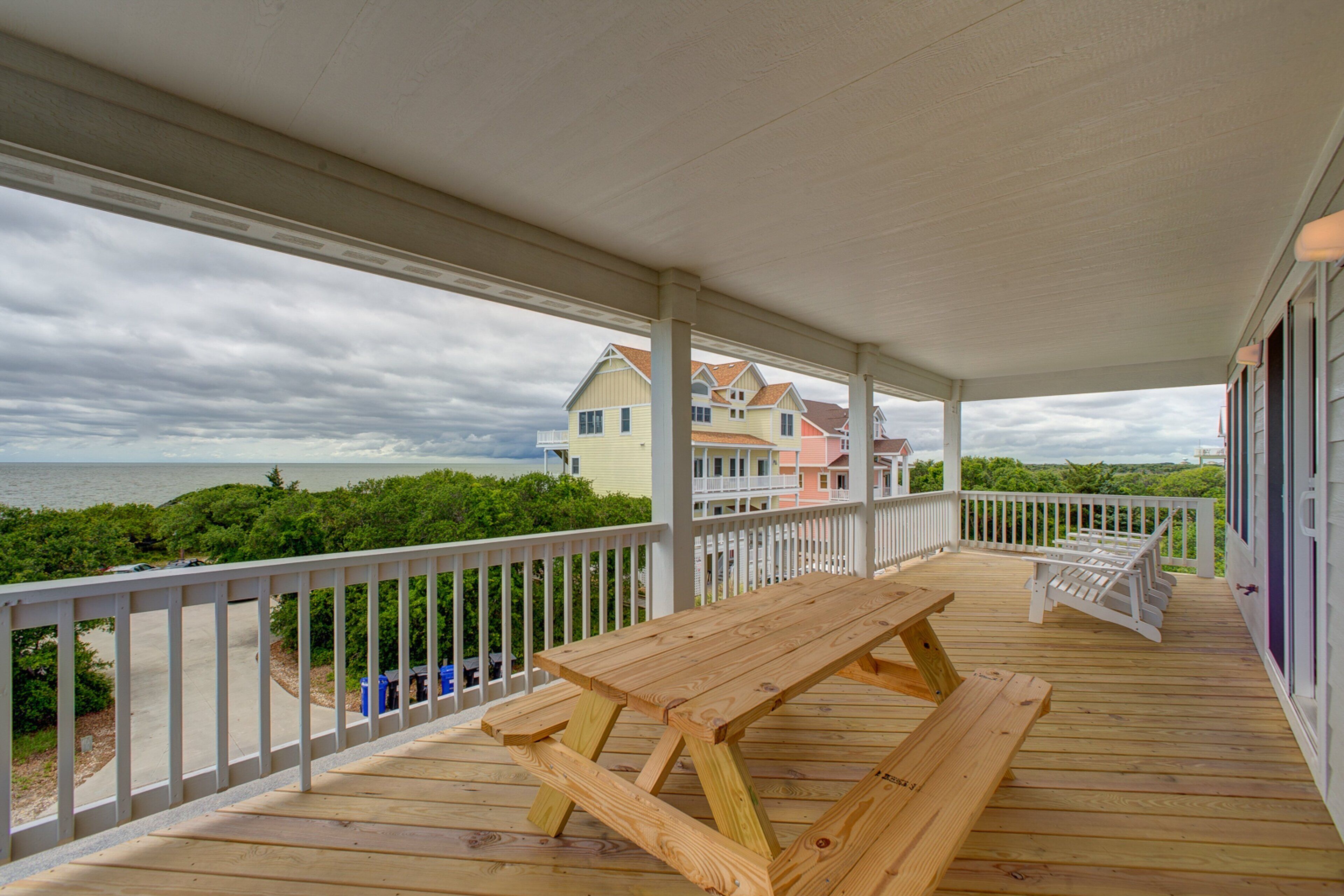 A wooden deck with a picnic table and chairs, overlooking a body of water and houses.
