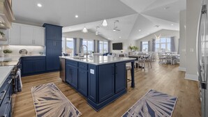 A modern kitchen with a large island, dark blue cabinets, and wooden flooring. - Oceanview Home with private pool and close beach access (North Topsail Beach)