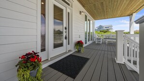A covered porch with a wooden ceiling, white railings, and a black doormat. - Oceanview Home with private pool and close beach access (North Topsail Beach)