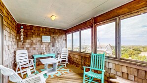 A covered porch with wooden walls, a table, chairs, and a view of the landscape. - Updated home with ocean & sound views, screened porch, balcony, pool access (Avon)