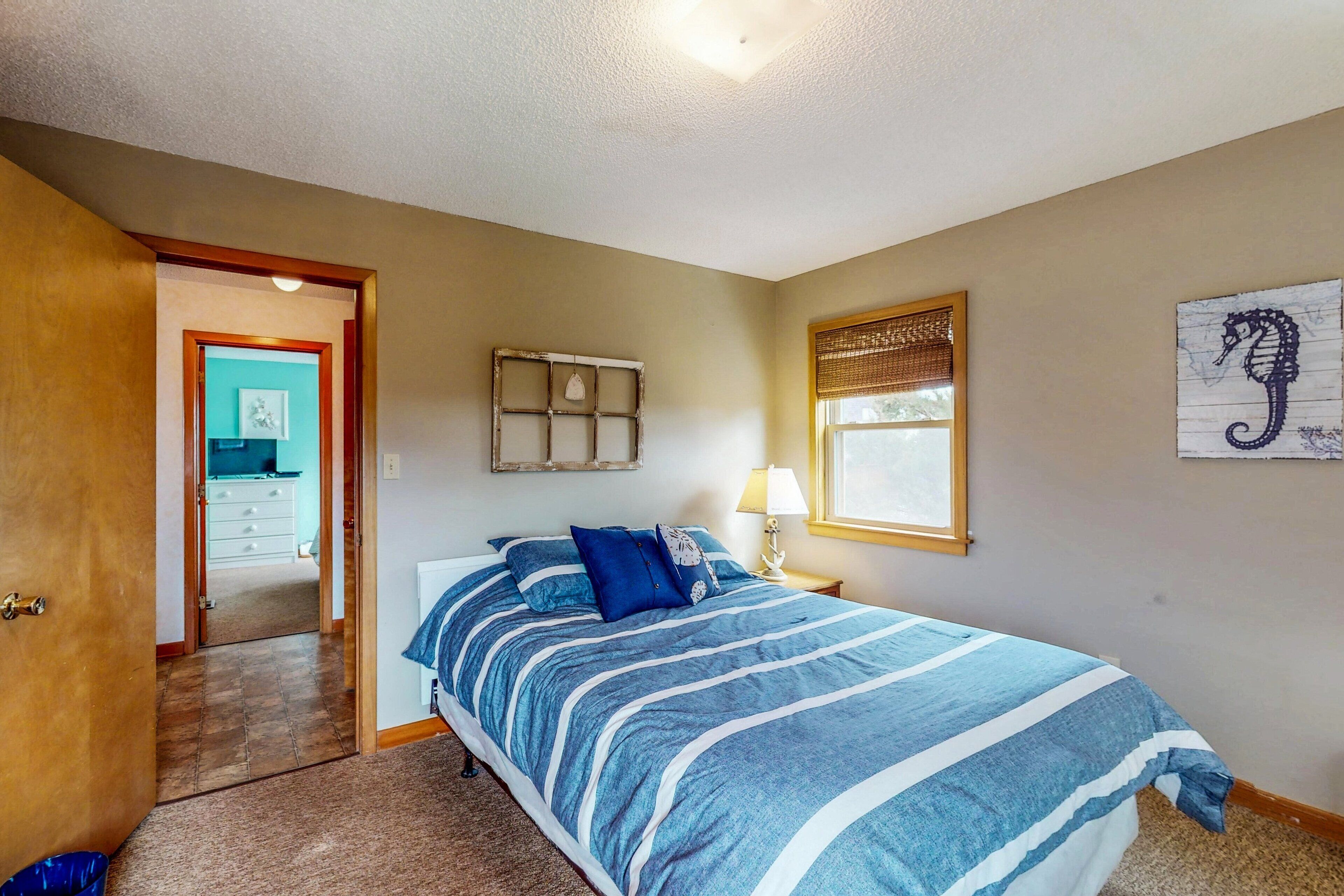 A bedroom with a bed, a nightstand, a window, and a door leading to another room.