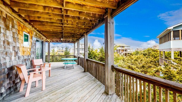 A wooden deck with chairs and a table, overlooking a forested area. - Updated home with ocean & sound views, screened porch, balcony, pool access (Avon)