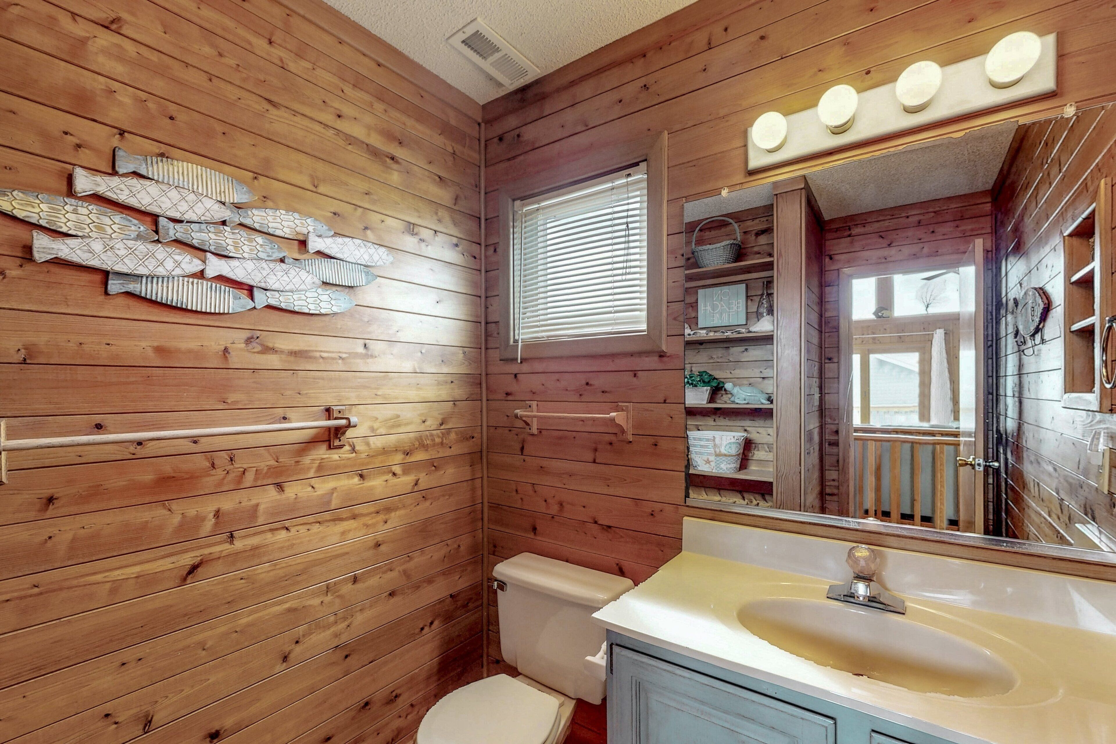 Un baño con paneles de madera, un inodoro, un lavamanos y un adorno de pared con motivos de peces.