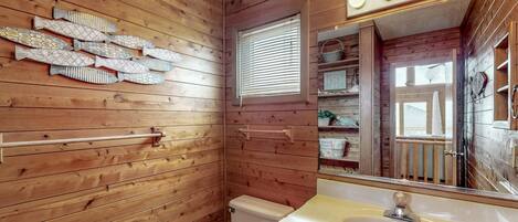 Un baño con paneles de madera, un inodoro, un lavamanos y un adorno de pared con motivos de peces.