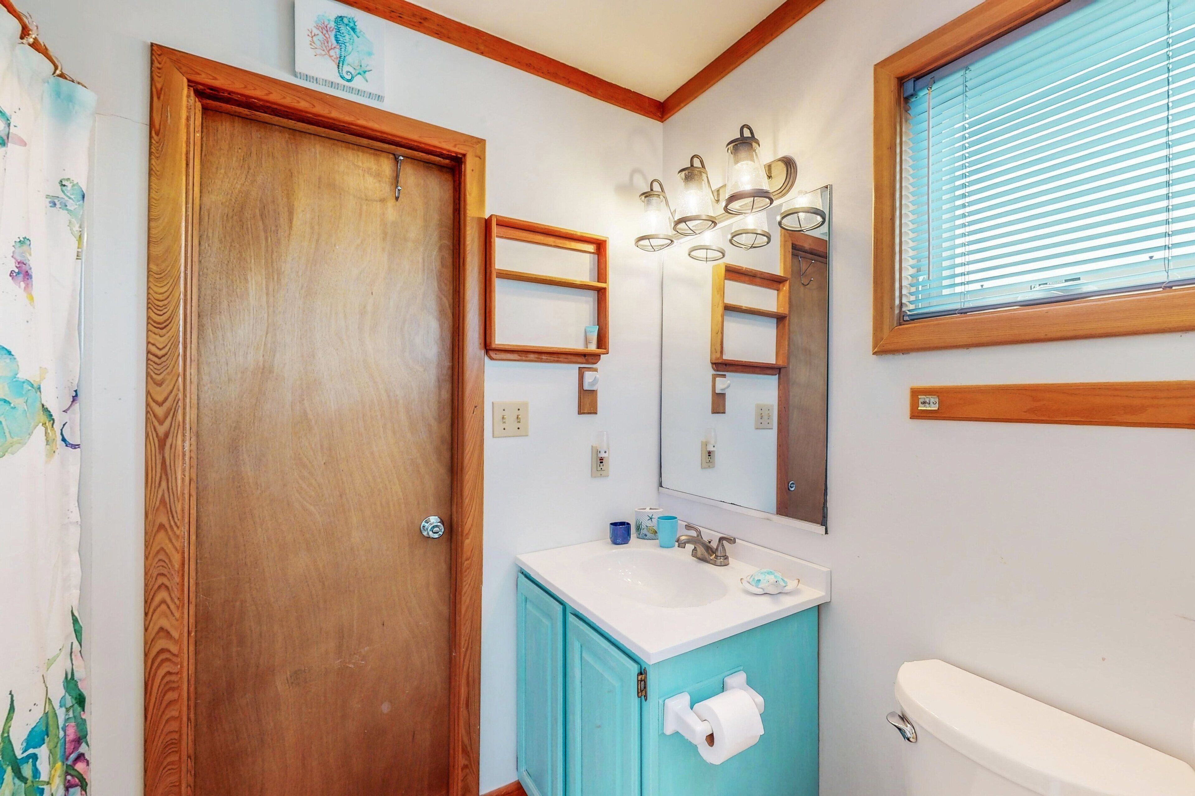 Een badkamer met een houten deur, een wastafel met een spiegel erboven en een toilet.