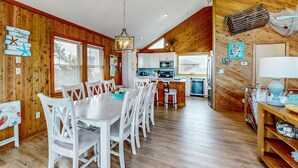 A spacious dining area with a wooden interior, a kitchen with white cabinets, and a view of the outdoors. - Updated home with ocean & sound views, screened porch, balcony, pool access (Avon)