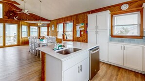 A kitchen with wooden walls, white cabinets, a central island with a sink, and a dining area with white chairs. - Updated home with ocean & sound views, screened porch, balcony, pool access (Avon)