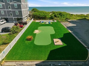 A golf course with a view of the ocean, a parking area with cars, and a building with multiple floors.