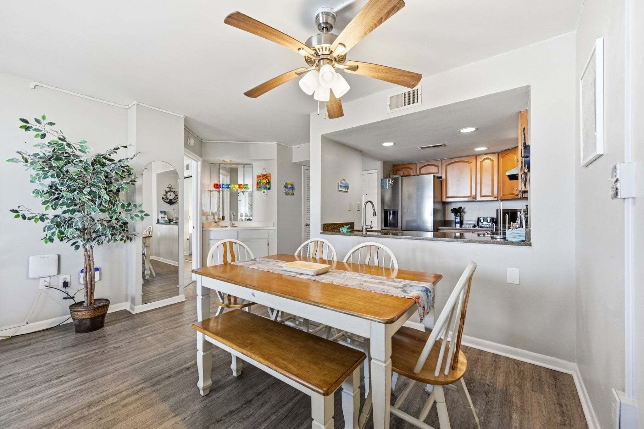 A dining area with a wooden table and chairs, a ceiling fan, and a potted plant.