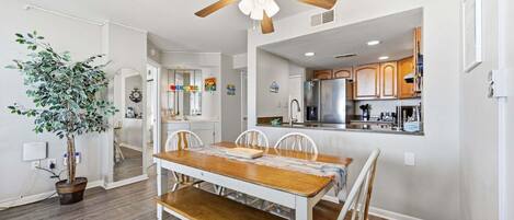 A dining area with a wooden table and chairs, a ceiling fan, and a potted plant.