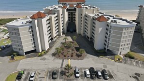 A multi-story hotel with a central courtyard, parking lot, and a view of the beach. - Oceanfront condo with shared pool, shared sauna and beach access (North Topsail Beach)