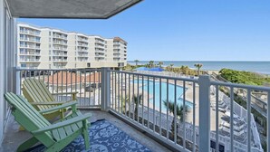 A balcony with a view of a swimming pool, beach, and hotel buildings. - Oceanfront condo with shared pool, shared sauna and beach access (North Topsail Beach)